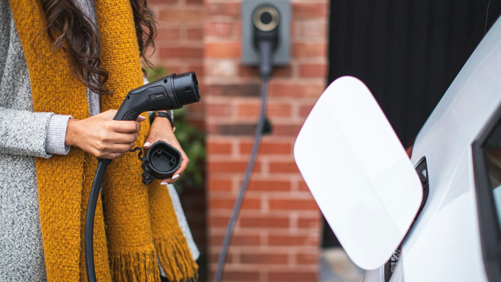 A woman holding an electric vehicle charger next to an EV.