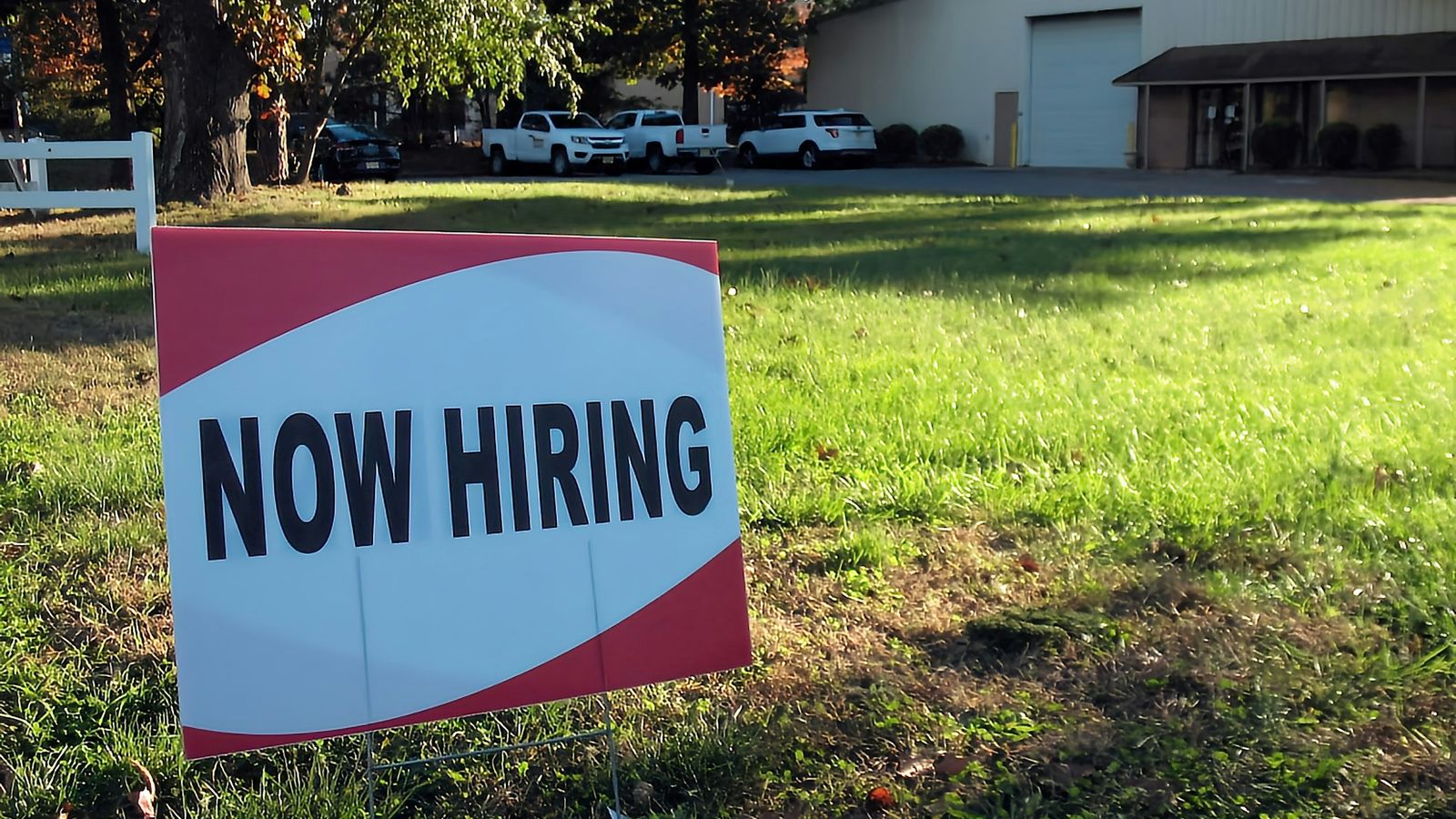 A now hiring sign in a lawn.