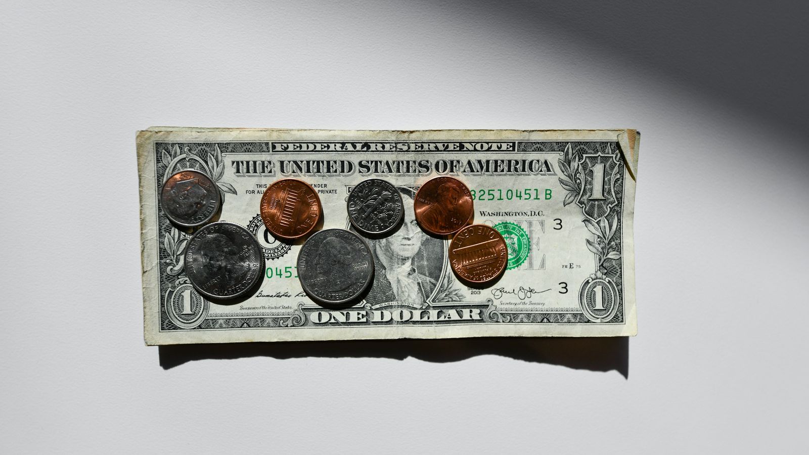A dollar bill with quarters, dimes, and pennies on top.