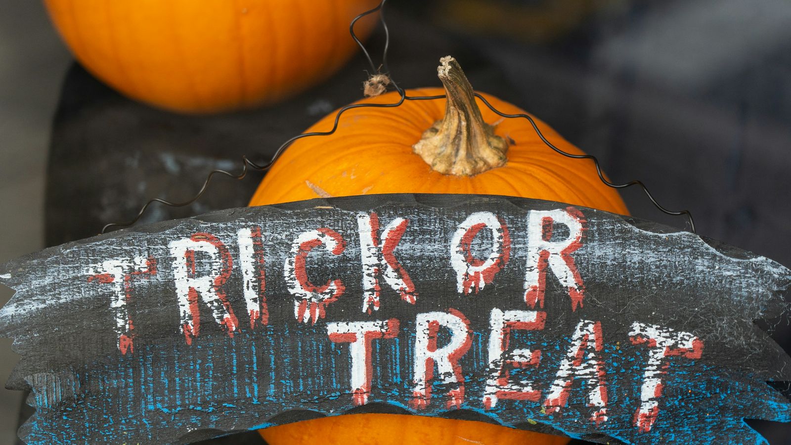 A trick or treat sign in front of pumpkins.