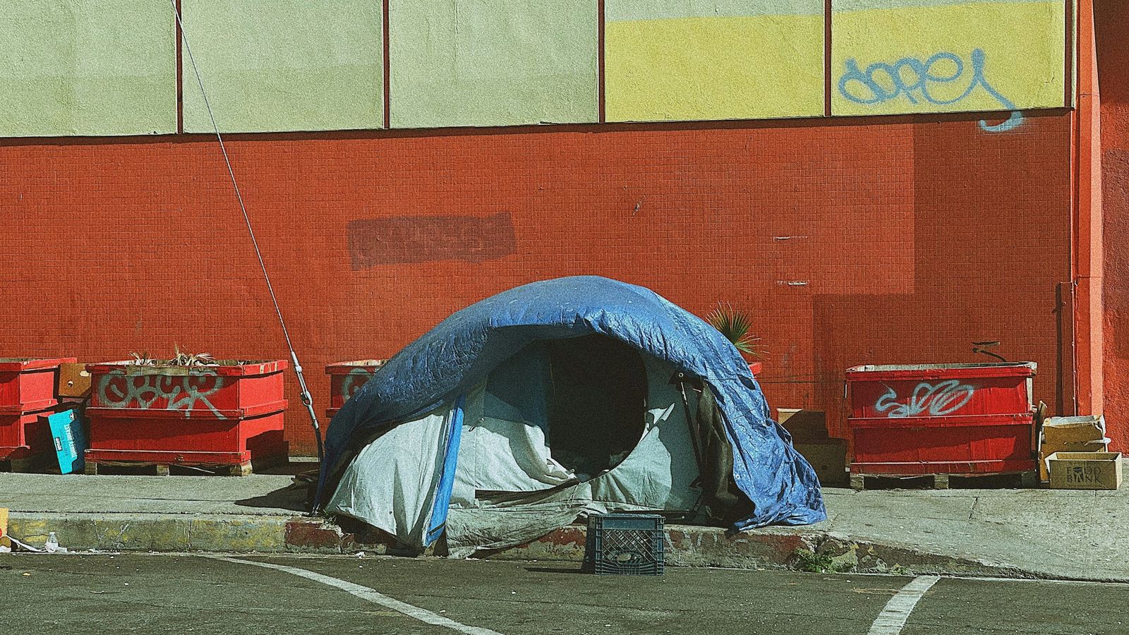 A tent pitched outside a building with graffiti.